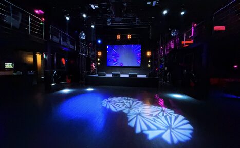 Арендовать Castle Concert Hall(Концертный зал Замок). Большое тёмное помещение с сценой и экраном. Металлические балконы по бокам, диско-шары, разноцветное освещение с узорами на полу. Черный пол, высокий потолок, световые приборы, цветная подсветка. Монохромная и фиолетовая гамма.