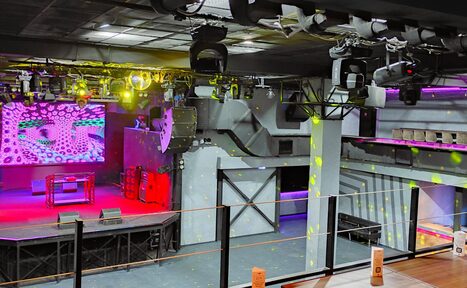 Арендовать PRAVDA(Правда). Просторный зал на 800 гостей. Концертный зал с большим экраном на стене, DJ-стойкой и световым оборудованием. Серые стены, черный потолок с видимыми коммуникациями, разноцветные прожекторы. Танцпол с ограждением, балкон с барными стойками. Пространство в индустриальном стиле.