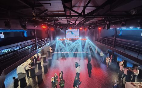 Арендовать СВОБОДА. Зал на 1200 человек. Просторная комната с высокими потолками, оснащена сценой с подсветкой и большим экраном. Вокруг расставлены высокие круглые столы с белыми скатертями. На полу паркет, по периметру полумрак с ярким светом на сцене.