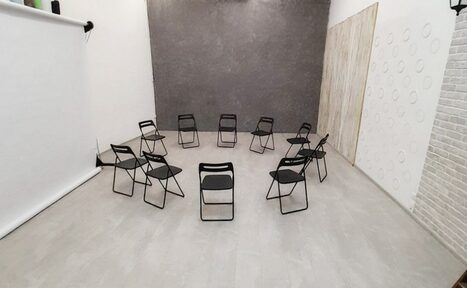 Арендовать Интер-Фото. Пространство с серыми стенами и светлым полом. Расставлены черные складные стулья по кругу. Справа белая стена с круглыми узорами, слева белый экран. Одна стена имитирует кирпич, другая - дерево. Освещение невидимо.