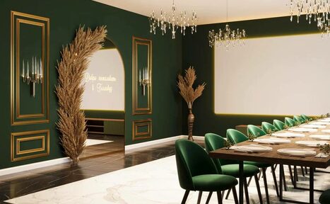 Арендовать Голливуд. Элегантный лофт в зелено-бежевых оттенках. Пространство с длинным столом и зелёными стульями. Тёмно-зелёные стены с золотыми рамками. На полу бело-коричневый мрамор. Подвесные люстры, неоновая надпись, декоративные растения. Арочный проход. Светлое потолочное освещение.