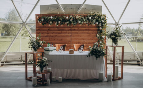 Арендовать Эко-отель "Джао Да!Ча". Шатер-Сфера. Шатровое помещение с треугольными окнами, деревянная стена с гирляндой из зелени и цветов, белый стол с белой скатертью, стеклянные декоративные элементы, свечи, бокалы, столовые приборы, декорации из живых растений.