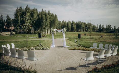 Арендовать Эко-отель "Джао Да!Ча". Шатер-Сфера. Открытое пространство для мероприятий на улице, с каменной дорожкой, расположенной между двумя рядами белых стульев. В центре арка с белой тканью и цветами. Вокруг травяной газон и деревья. Установлены две колонки на стойках.