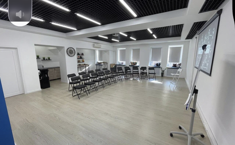Арендовать Уютный тренинговый зал на Таганской. Современное светлое помещение с деревянным полом, расставлены черные складные стулья в два ряда. Справа — флипчарт, слева — проем в небольшую зону с раковиной и полками. Потолок с черными панелями и встроенным освещением. Белые стены, окна с жалюзи.