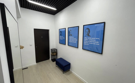 Арендовать Уютный тренинговый зал на Таганской. Узкий коридор с белыми стенами и светлым деревянным полом. Черный подвесной потолок с встроенным светильником. Три синие картины на стене, черная дверь, синяя скамья и черный декор на полу.