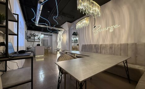 Арендовать Лофт SUNRISE(Восход Солнца). Просторное помещение на 15 гостей. Пространство с длинным столом и стульями, мягкими стеновыми сидениями. На стене неоновая вывеска. Потолок с видимыми коммуникациями, декоративное освещение. Пол из плитки. Современный интерьер.