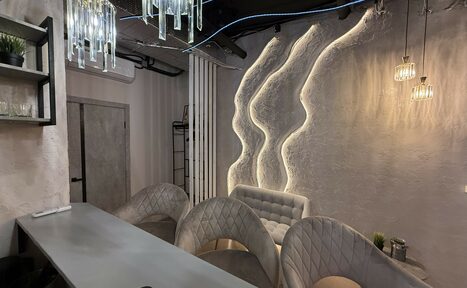 Арендовать Лофт SUNRISE(Восход Солнца). Просторное помещение на 15 гостей. Лофт-пространство с барной стойкой и барными стульями, светло-серая обивка, кованая металлическая стена с подсветкой, мягкое освещение, декоративные подвесные лампы, открытые вентиляционные трубы, полки с растениями.