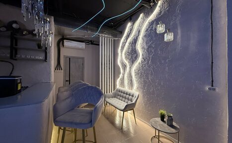 Арендовать Лофт SUNRISE(Восход Солнца). Просторное помещение на 15 гостей. Современное помещение с барной стойкой и мягкими стульями. Стены с акцентным освещением и фактурной отделкой, подвесные стеклянные светильники, обивка мебели в серых тонах, стеклянный столик с декором, бежевый пол, кондиционер и видимые трубы на потолке.