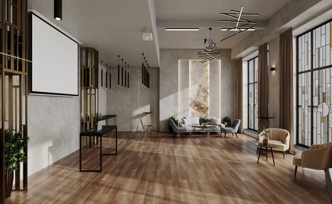 Арендовать Лофт Мираж. Просторное помещение с деревянным полом, светло-серыми стенами и большими окнами. Угловой диван с журнальным столиком, несколько стульев. Подвесные светильники, проектор и экран. Декоративные элементы, растения у стены.