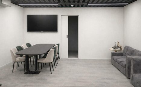 Арендовать Level 5(Лэвел 5). Современная переговорная комната с длинным черным столом и восьми стульями. На стене большой экран. Справа серый диван и небольшой столик с аксессуарами. Светлые стены, пол из светло-серого материала, потолок темный с освещением.