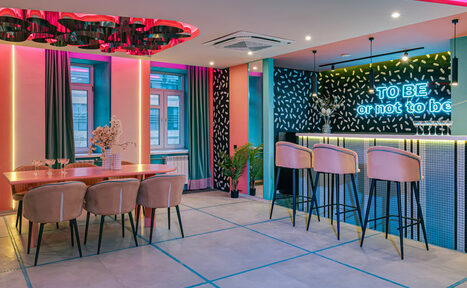 Арендовать Лофт Шекспир. Стильный дизайнерский зал. Современное пространство с обеденной зоной и барной стойкой. Зал украшен неоновыми надписями, имеет яркую цветовую подсветку. Мебель включает длинный стол с креслами и барные стулья. На стенах контрастные узоры. Пол из светлой плитки.