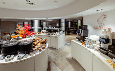 Арендовать Итальянский ресторан Umberto(Умберто). Современное кафе с круглой барной стойкой, сервированной выпечкой и фруктами. Светлые стены, стеклянные дисплеи, кофемашина, посуда. Освещение встроенными светильниками. На стене световой декор. Пол из светлой плитки.