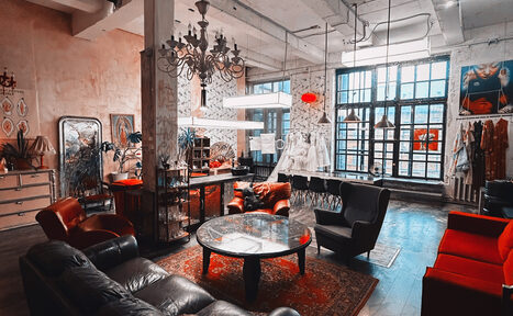 Арендовать Лофт Делюкс. Лофт-пространство с высокими потолками и большими окнами. В центре круглые стеклянные столы, окруженные кожаными креслами и диванами. Присутствуют шкафы, зеркала и декор на стенах. Освещение от разнообразных люстр и подвесных ламп.