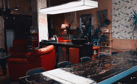 Арендовать Лофт Делюкс. Лофт-пространство с открытой планировкой. Красные кресла, длинный стол, подвесное освещение. Декор: картины, растения. Стены нейтральных тонов, часть с узором. Присутствуют кухонные элементы. На стене надпись "Love".