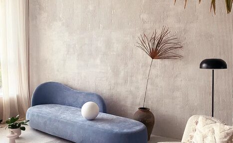 Арендовать Киото. Светлый зал с кухней. Современное жилое пространство с бежевыми текстурированными стенами, голубым диваном необычной формы, белым шаром-декором, светлой мебелью, настольной лампой, растением в вазе и мягким естественным освещением через полупрозрачные шторы.