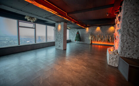 Арендовать ATMOSFERA 53(Атмосфера 53). Просторное помещение с панорамными окнами и темным полом. На стенах декоративные элементы с растениями, светодиодная иллюминация. Потолок с акцентным освещением. Угловая стена оформлена камнем, присутствует елка и вазы с высокими травами.