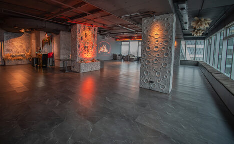 Арендовать ATMOSFERA 53(Атмосфера 53). Просторное помещение с колоннами, облицованными узорчатым материалом. Пол темный, глянцевый. На стенах проекция с изображением. Большие окна, скамьи вдоль них. Несколько зон с диванами и столами. Потолок открытый, индустриального стиля.