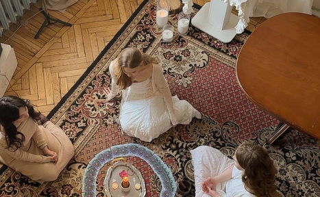 Арендовать Студия Свети. Пространство с паркетным полом и ковром с узором, круглый столик с декоративными свечами. Три человека сидят на ковре. Светлые и темные тона в интерьере, свечи добавляют мягкое освещение.