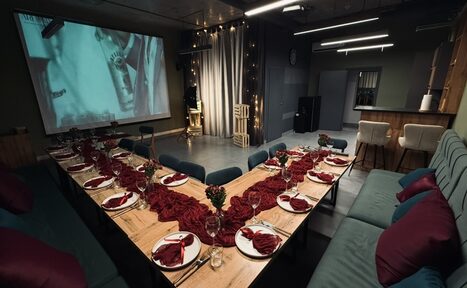 Арендовать Лофт Интра. Зал Фрей. Зал для мероприятий с экраном и проектором, U-образная расстановка столов, деревянные столы с сервировкой; красочные салфетки, бокалы и тарелки. Мягкие диваны и стулья. Подвесные светильники, нейтральные тона, темные шторы, декоративные огни.