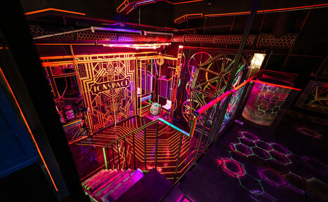 Арендовать Лофт Космос. Зал Ночной Клуб. Клубное помещение с лестницей, оформленной в неоновом стиле. Яркие разноцветные полосы и узоры на стенах и полу. Металлические перила, множество неоновых ламп, тёмная цветовая гамма с акцентами красного, синего и жёлтого цветов.