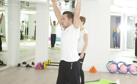 Арендовать Face & Body(Лицо и Тело). Фитнес-студия с зеркальными стенами, паркетным полом и ярким освещением. В зале находятся коврики для йоги, гантели, разноцветные фитнес-мячи и прыжковые резинки. Люди занимаются физическими упражнениями.