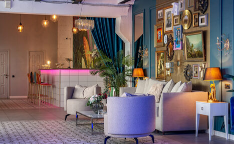 Арендовать Лофт Май. Стильное пространство с верандой. Просторное помещение с зоной отдыха и барной стойкой. Диваны и кресла серых оттенков, журнальный столик, декоративные подушки. Яркие настенные картины и зеркала. Подвесные светильники, лампы. Бар с розовой подсветкой, стулья. Плиточный пол с узором.