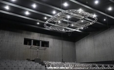 Арендовать Театр в Хамовниках. Зал с амфитеатром, серые ступенчатые ряды кресел, тёмный рельефный потолок с лампами, подвесная металлическая конструкция, стены отделаны вертикальными панелями серого цвета.