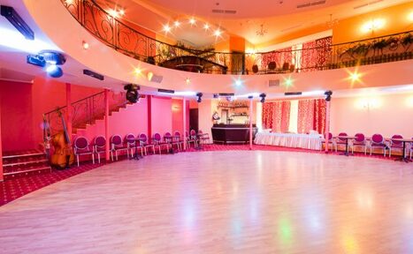 Арендовать Jenavi CLUB(Дженави Клуб). Пространство с круглой планировкой, паркетный пол, по периметру розовые стулья, два уровня с перилами и лестницей слева, барная стойка, яркое освещение с цветными лампами, стены розового и оранжевого цвета, задрапированные окна.