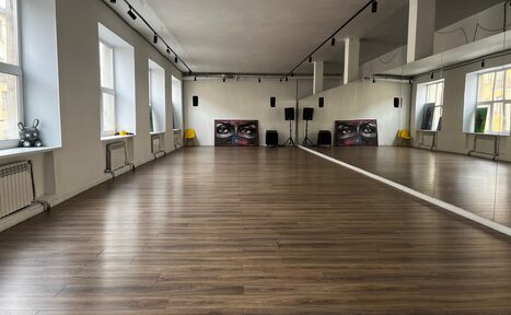 Арендовать The Flow Space(Пространство Поток). Просторная комната с деревянным полом и большими окнами вдоль стены. На одной стене — зеркало во всю длину. На дальнем конце — звукосистема и настенные панели с изображением глаз. Помещение хорошо освещено, светлые стены, черные светильники на потолке.