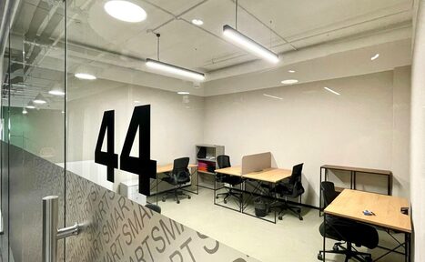 Арендовать Smart Coworking(Умный Коворкинг). Офисное помещение с бежевыми стенами. Четыре стола и кресла, полки для документов. Стеклянная дверь с номером "44". Потолочные светильники. Ламинат серого цвета на полу. На стекле повторяющийся текст "SMART".