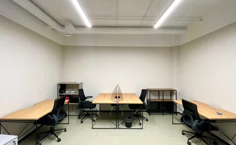 Арендовать Smart Coworking(Умный Коворкинг). Офисное помещение с пятью рабочими местами. Планировка линейная с расположением столов вдоль стен. Каждый стол оснащён чёрным офисным креслом. Светлые стены и пол, нейтральное освещение, параллельные потолочные светильники.