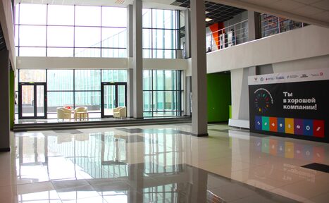 Арендовать Конференц-зал площадью 17000 м² до 280 гостей. Современное просторное помещение с большими окнами и стеклянными дверями. Пол из плитки, белые колонны. В углу кресла и столик. Стены зеленого и белого цвета. На стене панель с текстом «Ты в хорошей компании!» и цветными иконками.