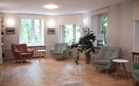 Арендовать Музыкальная гостиная Научно-просветительского центра Музея М.А. Булгакова. Светлая комната с паркетным полом, тремя креслами пастельных тонов, белыми круглыми столиками. На стенах картины. Большие окна с видом на деревья. Комнатные растения, натуральное и искусственное освещение.