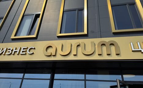 Арендовать АТRIUМ НАLL (Атриум Холл) . Фасад здания с окнами в золотых рамах на сером фоне. Вывеска с текстом "Бизнес aurum Центр" на золотой панели. Входная дверь внизу справа.