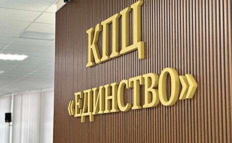 Арендовать КПЦ Единство. Стена с вертикальными деревянными панелями, украшена объемными золотыми буквами с текстом "КПЦ ЕДИНСТВО". На заднем плане видна часть потолка с плафоном и колонна.