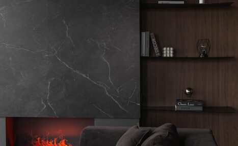 Арендовать Зал Black. Фотостудия Мимика. Современная гостиная с черным мраморным камином, создающим эффект пламени. Справа деревянные полки с книгами и декором. Спереди темный диван с подушками. Темные, нейтральные оттенки и минималистичный стиль.