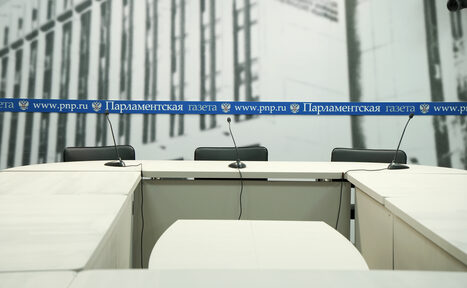 Арендовать Медиацентр Парламентской газеты. Конференц-зал с белыми столами, микрофонами на стойках, черными офисными стульями. На заднем плане серый графический фон с вертикальными линиями. На столах синяя полоса с текстом: "Парламентская газета www.pnp.ru".