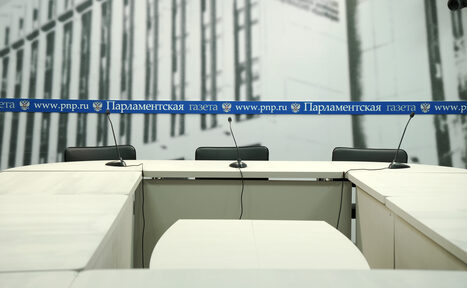 Арендовать Медиацентр Парламентской газеты. Конференц-зал с тремя креслами и белыми столами, стоящие буквой "П". На столах размещены микрофоны. На стене фон с изображением архитектуры и полосой с текстом "www.pnp.ru" и "Парламентская газета".