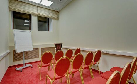 Арендовать Бородино Конгресс-отель. Зал Воронцов. Небольшое помещение в виде аудитории с девятью красными стульями в три ряда. Справа на стене установлены розетки, слева — флипчарт. На полу красный ковер, стены бежевые. Под потолком два окна с жалюзи. Освещение потолочное.