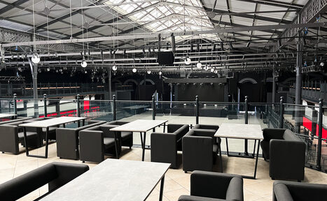 Арендовать Концертный зал площадью 2500 м² до 2200 гостей. Loft-стиль помещение с открытой планировкой, металлические конструкции, стеклянные перегородки. Мебель: серые столы и чёрные кресла. Металлический каркас крыши, подвесные светильники. Светлые плиточные полы. Виден верхний ярус и сцена внизу.