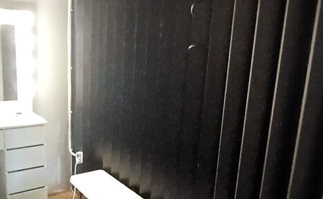 Арендовать Фитнес студия в почасовую аренду. Комната с туалетным столиком и зеркалом с подсветкой слева, белым стулом и большой темной ширмой справа. На полу деревянное покрытие. Стены светлые, присутствует кабель, соединенный с розеткой.