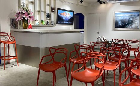 Арендовать Светлое пространство 68 м2. Просторное помещение с барной стойкой и множеством красных стульев. Стена украшена картинами и полками с предметами. Есть телевизор. Потолок оснащен трековыми светильниками, стены и потолок белые. На полу серое покрытие.