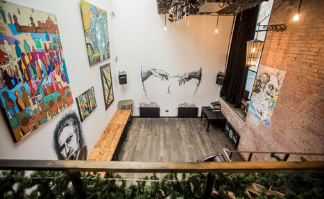 Арендовать Street Art Loft (Стрит Арт Лофт). Лофт-пространство с высокими потолками, стенами из белого кирпича и декором в виде граффити и картин. Деревянный пол, скамейки, столы, подвесное освещение, лестница. На стене розовый кирпич, черные шторы, нетекстовые знаки.