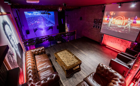 Арендовать Street Art Loft (Стрит Арт Лофт). Арт-пространство с диванами и журнальным столиком, проектор и экран с изображением, второй экран на стене. Кирпичные стены, деревянный пол, мягкая мебель из коричневой кожи. Красная неоновая подсветка, подвесные светильники, настенные картины.