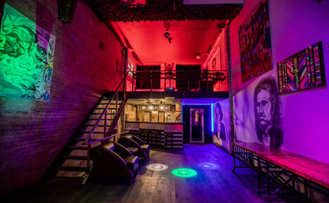 Арендовать Street Art Loft (Стрит Арт Лофт). Лофт с кирпичными стенами, деревянным полом и открытым потолком. Мезонин с металлическими перилами. Два кресла, длинная деревянная скамья, светильники, разноцветное освещение. На стенах красочные рисунки. Ступени из дерева и металла.