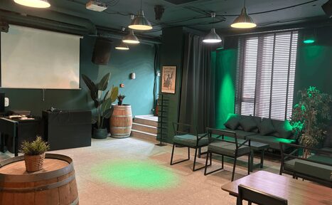 Арендовать Work Shop Loft(Воркшоп Лофт). Зал 11 . Многофункциональное пространство с проектором и экраном, деревянные бочки, диваны и столы. Стены и потолок тёмно-зелёного цвета. Лампы подвесные, окна с жалюзи. Есть декоративные растения и картина на стене.