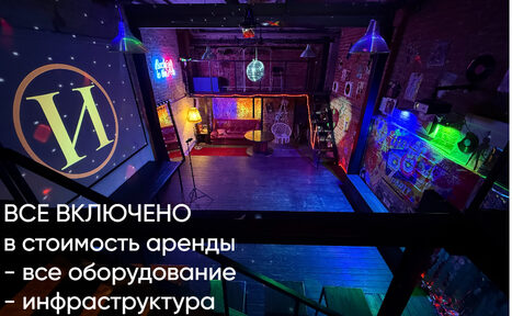 Арендовать Лофт ИЗНАНКА. Зал ЛИХИЕ 90-е. Затемнённая комната лофта, много людей в кадре проводят фуршетное мероприятие, беря еду с объединённых столов. Несколько людей на кадре танцуют