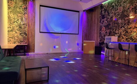 Арендовать Лофт для вечеринок с коктейльным баром . Просторное помещение с деревянным полом и ярким освещением. На стенах обои с цветочным узором. Имеется барная стойка со стульями, диван, стол, и большой экран. Светодиодные светильники создают разноцветные узоры на полу.