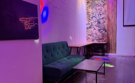 Арендовать Лофт для вечеринок с коктейльным баром . Лофт-пространство с мягким диваном и двумя деревянными столами. Стены белые с декоративными панелями и узорчатым акцентом. Небольшой металлический столик. Освещение разноцветное. На стене картина с абстрактным рисунком. Пол деревянный.