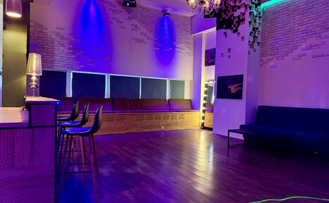 Арендовать Лофт для вечеринок с коктейльным баром . фото помещения: гостиная с барной стойкой, высокие стулья, диван, деревянный пол, стены из кирпича, люстра, голубое и фиолетовое освещение, черно-белое настенное панно, табурет.